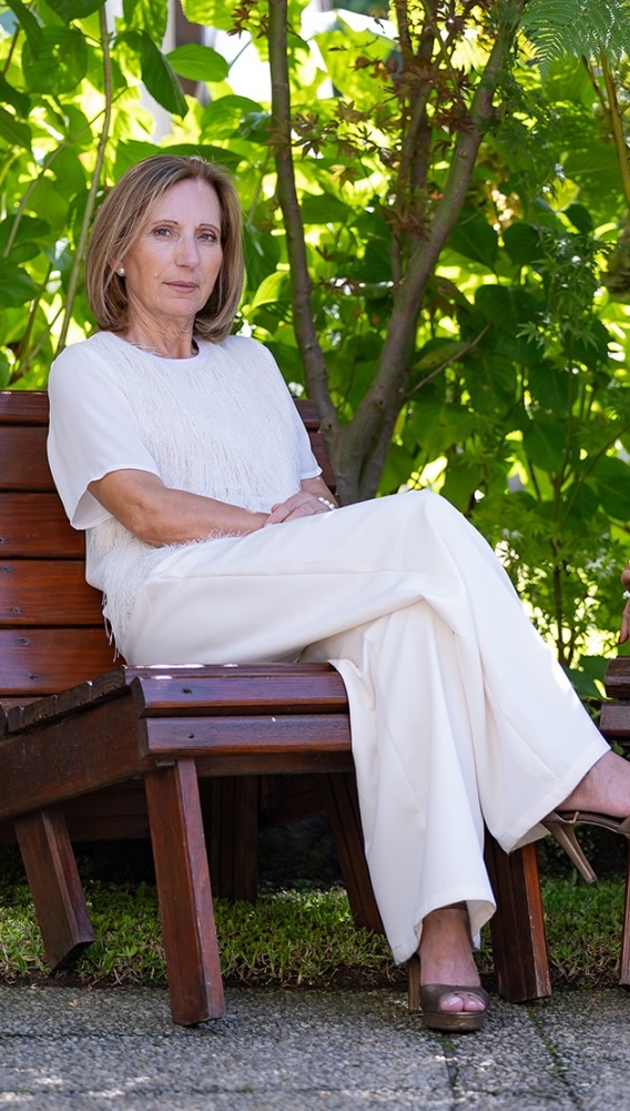 Sameiro Perestrelo sentada num banco de madeira num jardim, vestida de branco